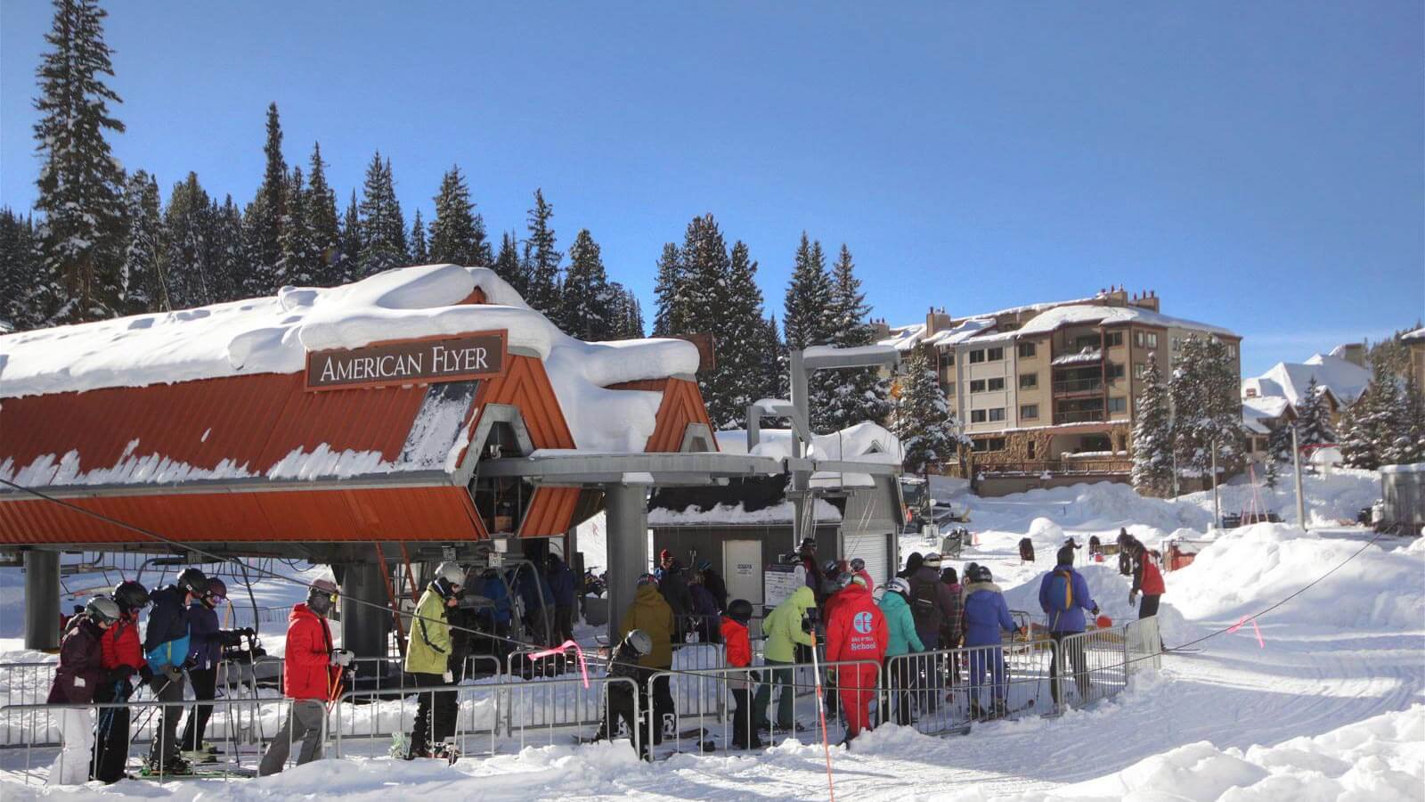 Skiers waiting in line at the American Flyer lift in Center Village at Copper Mountain on a sunny winter day.