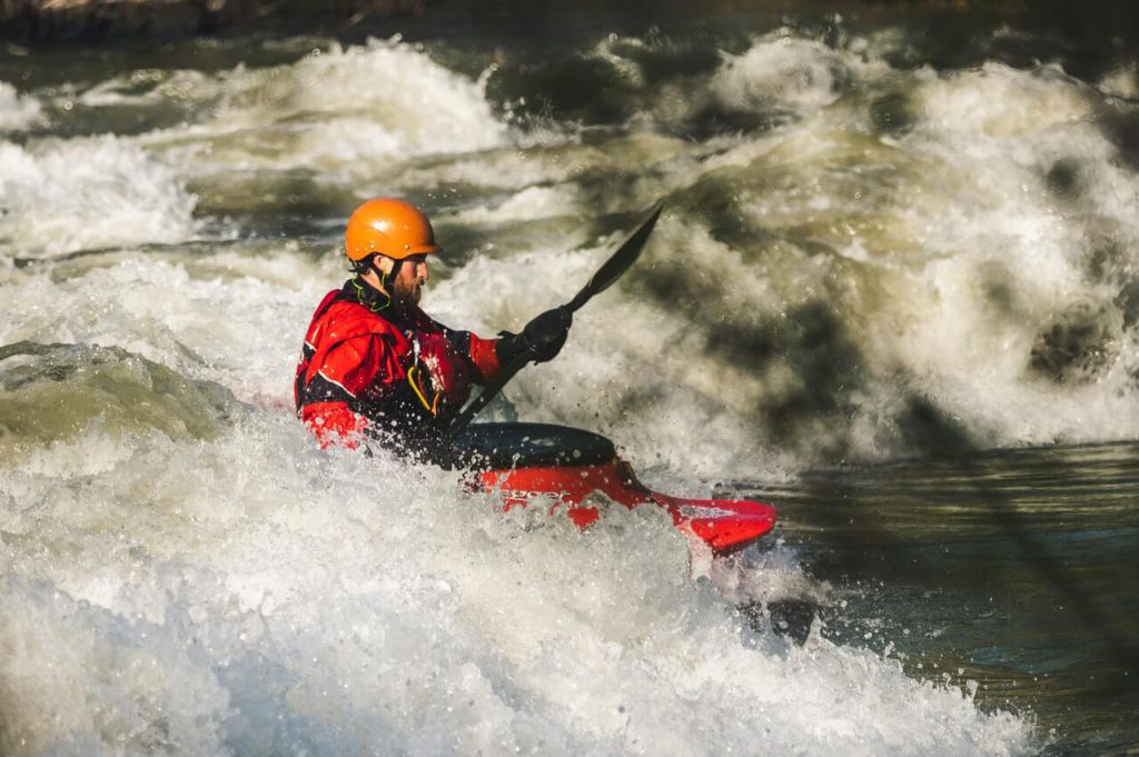 A person in a red suit and orange helmet white water rafting