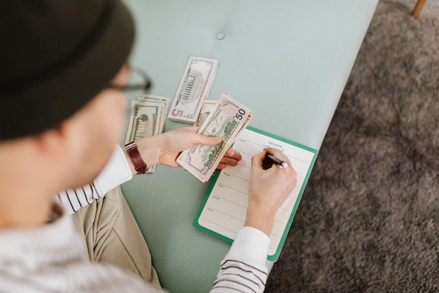 Person in hat counting money and noting down their spending budget