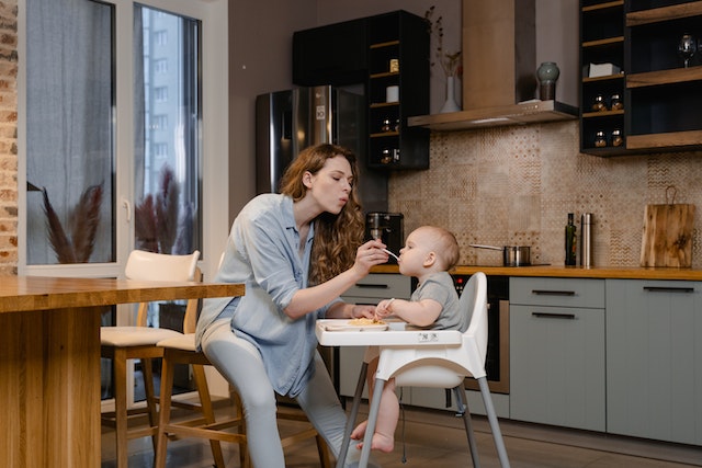 mother feeding their child who’s sitting in a highchair