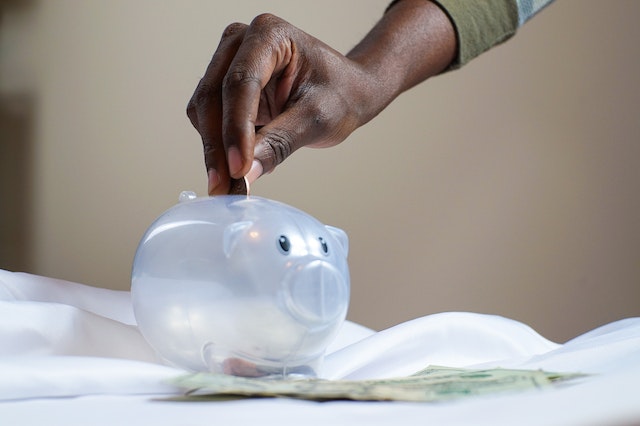 person placing a coin in a clear piggy bank